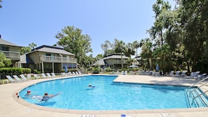 A swimming pool with lounge chairs and umbrellas, surrounded by buildings and trees. - Sunset Rentals | Tennismaster 801 | Dog Friendly (Hilton Head Island)