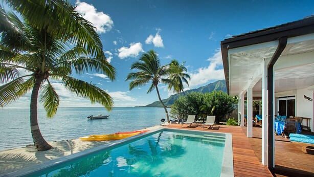 A pool area with a wooden deck, palm trees, and a view of the sea. - Villa TEPOE,  accès direct au lagon avec piscine et plage (Moorea-Maiao)