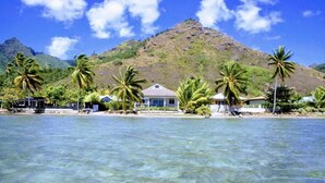 A beachfront property with clear water, palm trees, and a mountain in the background. - Villa TEPOE,  accès direct au lagon avec piscine et plage (Moorea-Maiao)