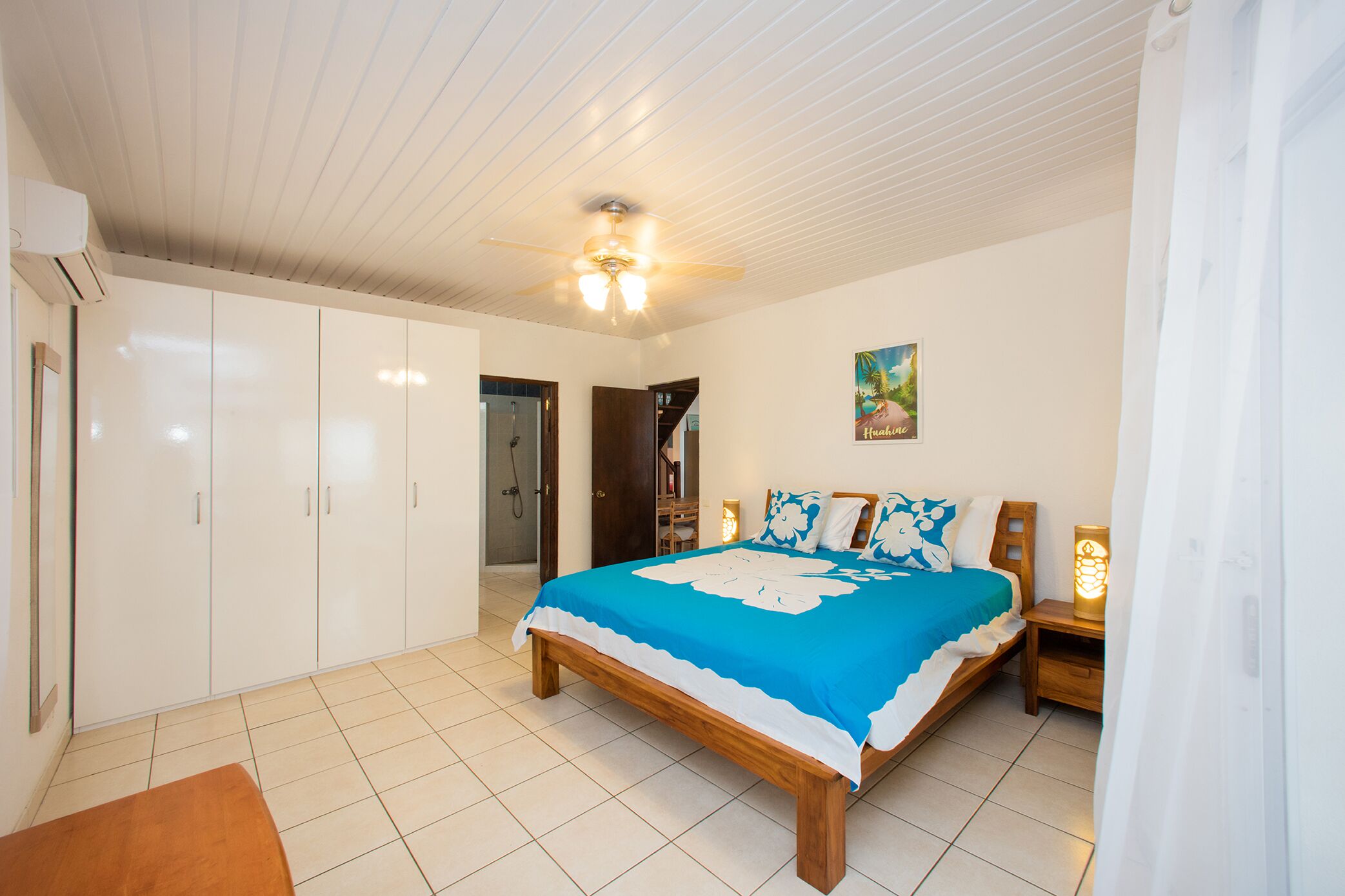 Une chambre à coucher avec un lit, une armoire, un ventilateur de plafond et un tableau accroché au mur.