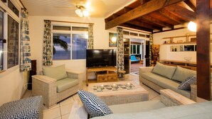 A cozy living room with wicker furniture, a flat-screen TV, and a view of the outdoors. - Villa TEPOE,  accès direct au lagon avec piscine et plage (Moorea-Maiao)