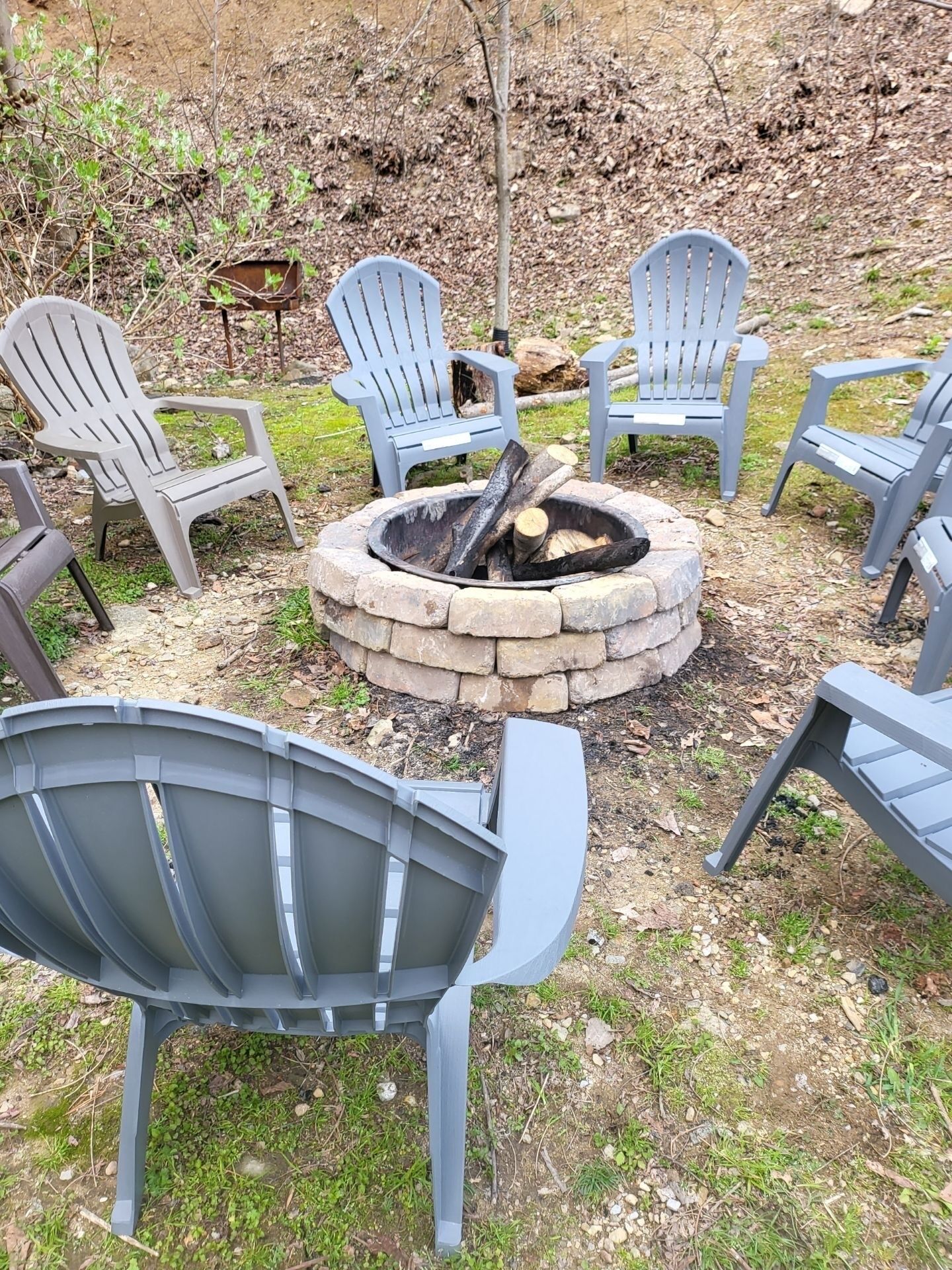 A fire pit surrounded by Adirondack chairs in a natural setting.