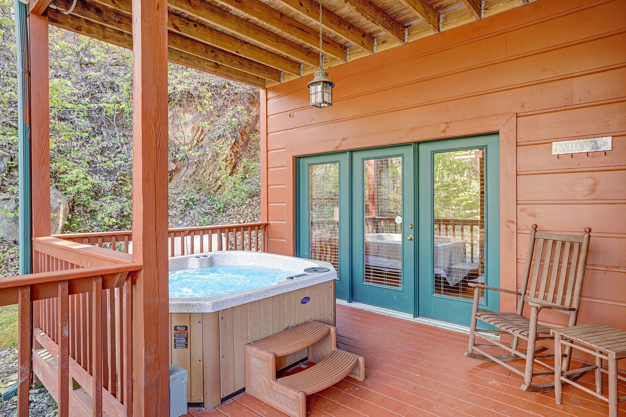 A wooden deck with a hot tub, a chair, and a door with a 'WELCOME' sign.
