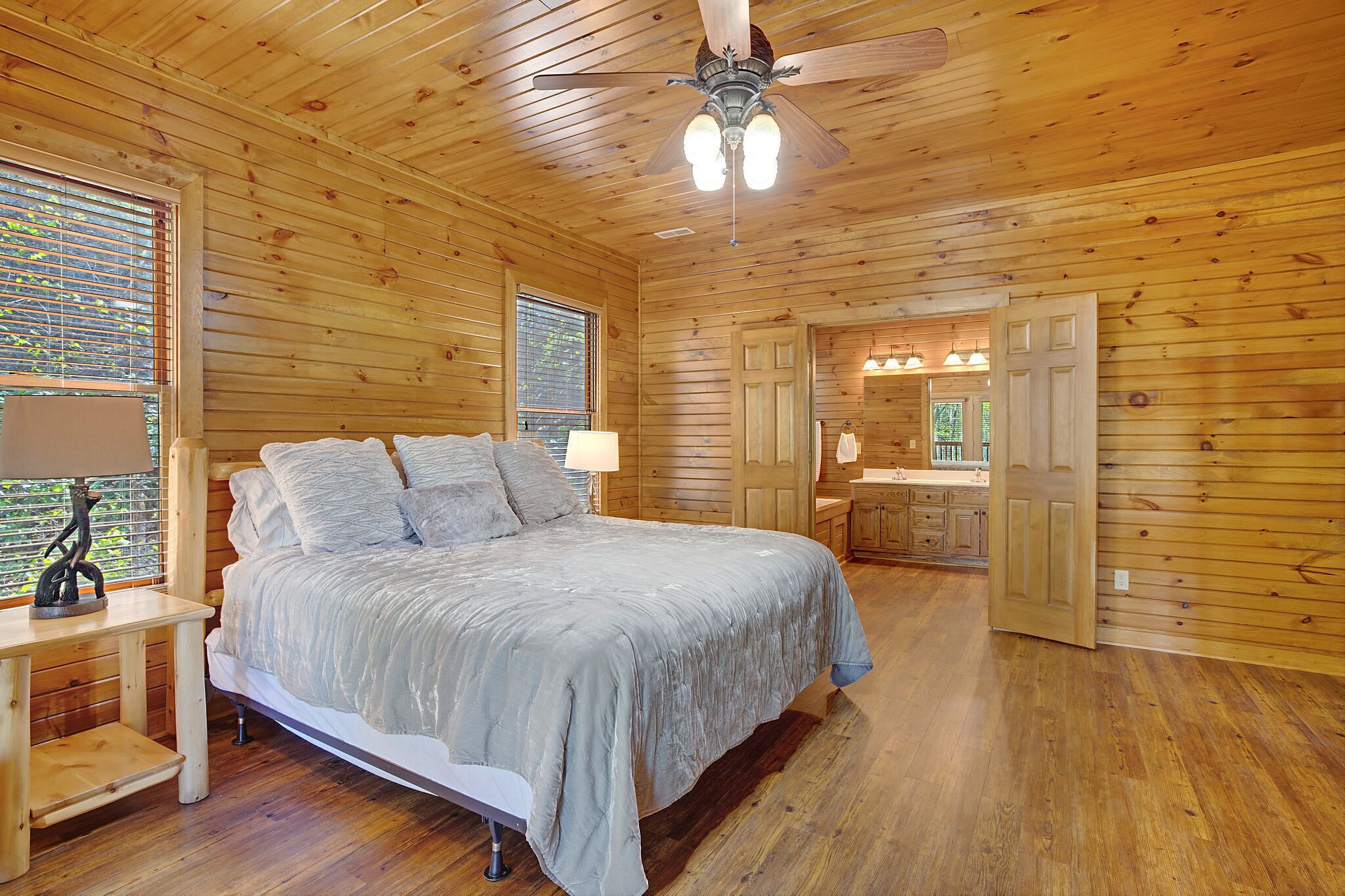 A wooden-paneled bedroom with a bed, bedside tables, and a ceiling fan.