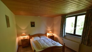 Une chambre à coucher avec un lit en bois, deux tables de chevet avec des lampes, un radiateur et une fenêtre avec des rideaux.