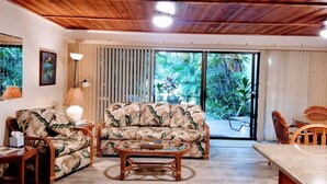 A living room with a wooden ceiling, a sofa, a coffee table, and a dining area with chairs.