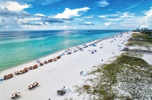 A beach with rows of umbrellas and lounge chairs, a pier in the background, and a clear sky. - Gulf Views-  Luxurious Amenities- Sleeps 4 Adults 2 Kids!  (Pensacola Beach)