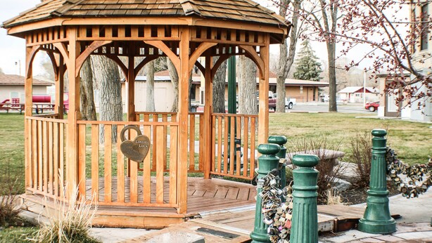 Un kiosque en bois avec un banc devant, entouré d’arbres et d’un lampadaire.