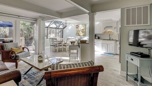 Un vaste espace de vie comprenant une table à manger, des chaises et un coin salon avec un canapé et un fauteuil. Il y a également une cuisine équipée de placards et d’un réfrigérateur.