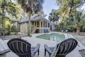 Une maison avec une piscine, deux fauteuils Adirondack et un patio couvert.