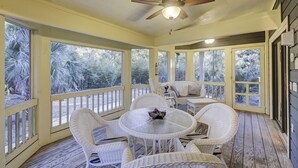 A covered patio with wicker furniture, a ceiling fan, and large windows overlooking a garden. - Sunset Rentals | Kingston Dunes 91 | Dog Friendly (Hilton Head Island)