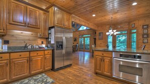 A spacious kitchen with wooden cabinets, stainless steel appliances, and a large window providing a view of the outdoors. - Black Bear River Lodge | Pet Friendly | Hot Tub | Creek Access (Epworth)