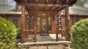 A log cabin with a wooden porch, a large front door, and a stone foundation. - Black Bear River Lodge | Pet Friendly | Hot Tub | Creek Access (Epworth)