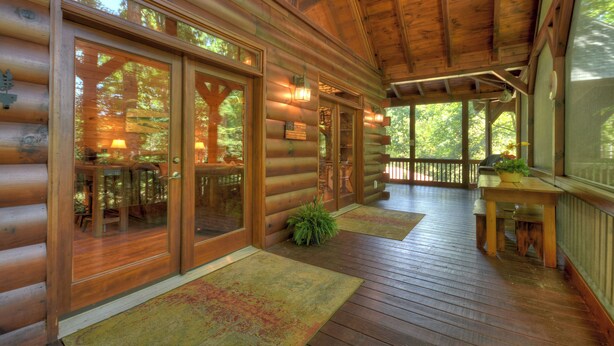 A log cabin with a wooden deck, large sliding glass doors, and a covered porch area. - Black Bear River Lodge | Pet Friendly | Hot Tub | Creek Access (Epworth)