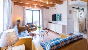 Un salon chaleureux avec un canapé, un fauteuil et une table, des poutres en bois au plafond, un téléviseur et une porte coulissante de style grange.