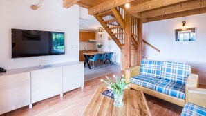 Un salon moderne doté d’un téléviseur à écran plat, de poutres en bois au plafond, d’un escalier et d’un canapé à motifs écossais.