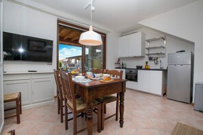 Une cuisine moderne avec des meubles blancs, une table à manger, des chaises, un téléviseur et une grande fenêtre.