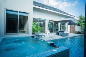 Una casa moderna con piscina, mobiliario exterior y un patio cubierto.
