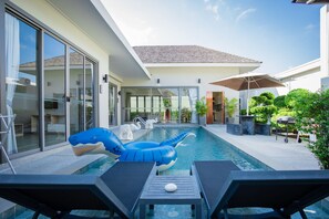 Un área de piscina moderna con un tiburón inflable azul, sillones de descanso y una vista despejada de la casa.