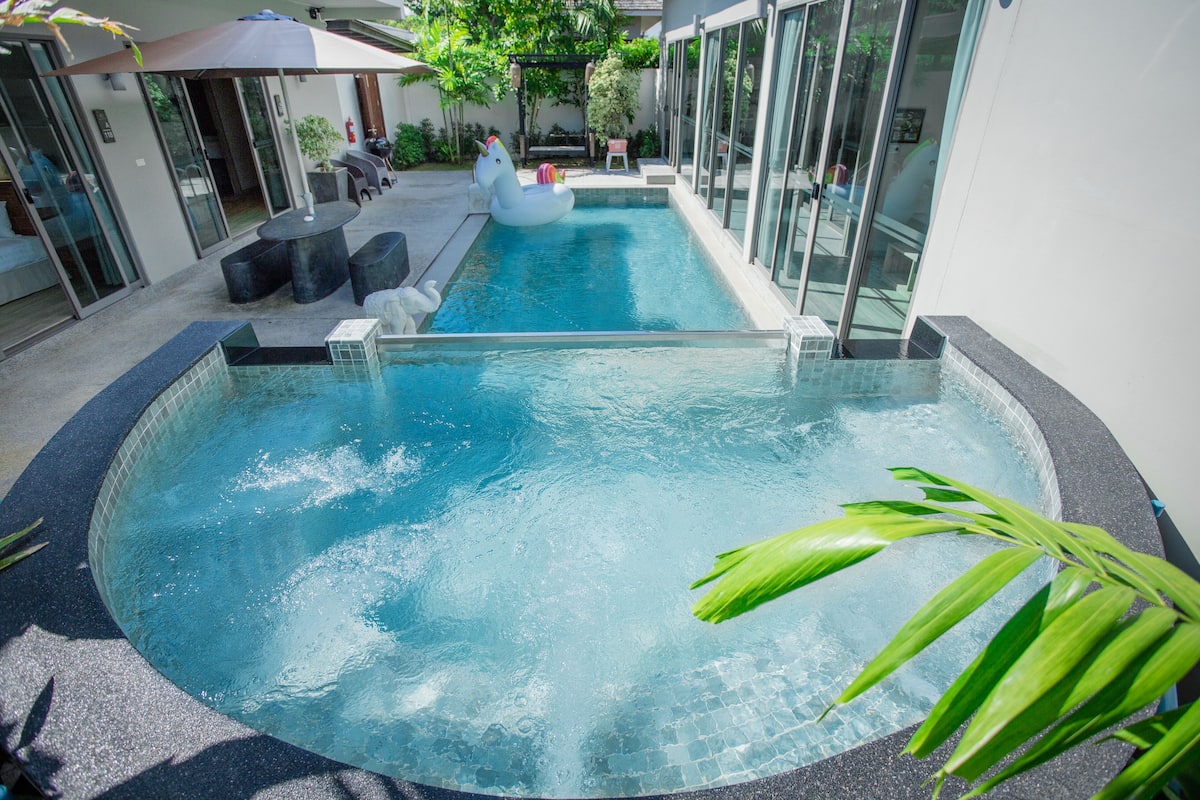 Ein Swimmingpool mit Glasrand, umgeben von Sitzgelegenheiten im Freien und einer überdachten Terrasse mit Glas.