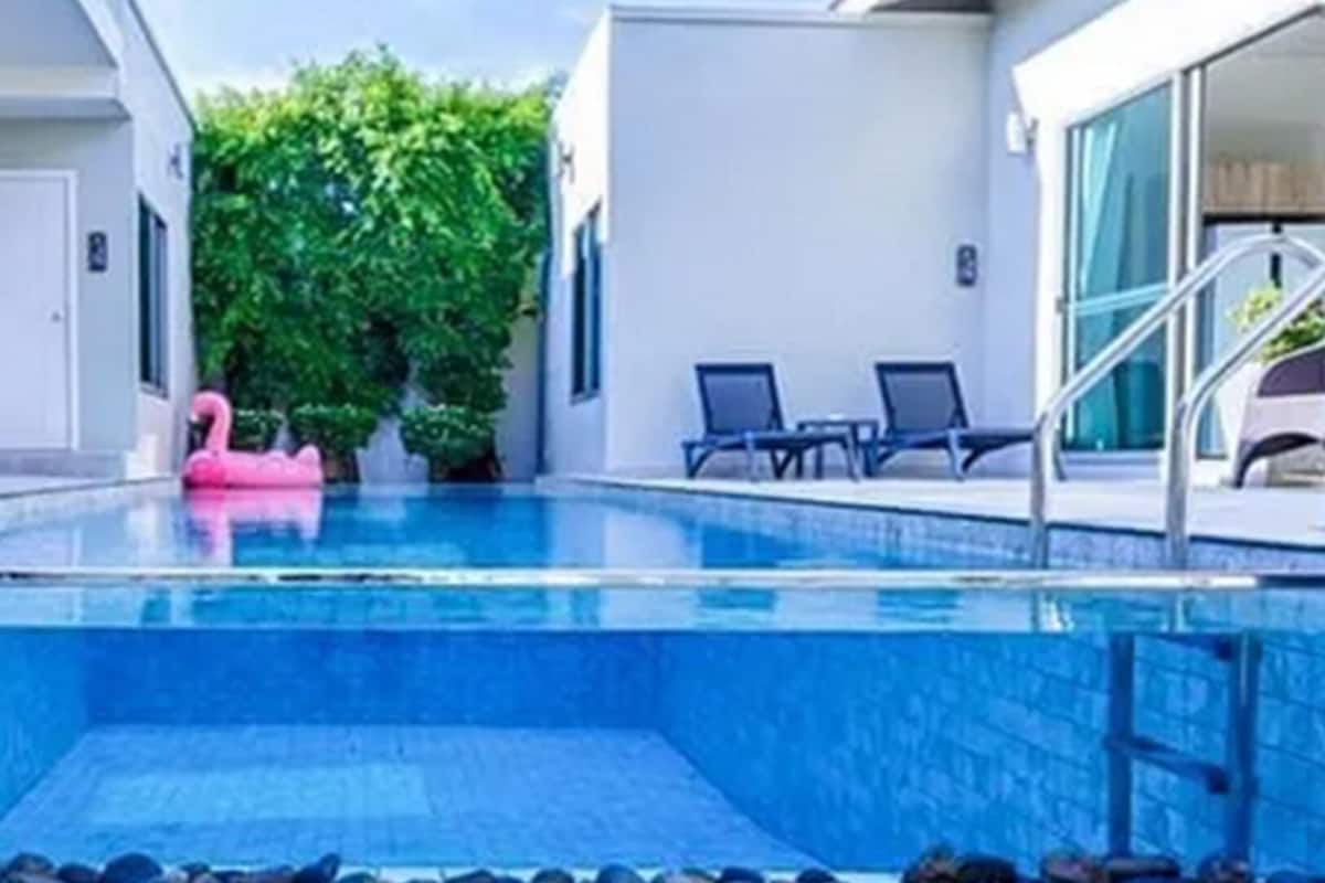 Ein Schwimmbecken mit einem rosa Flamingo-Schwimmspielzeug, Liegestühlen und einem überdachten Bereich mit einer Treppe.
