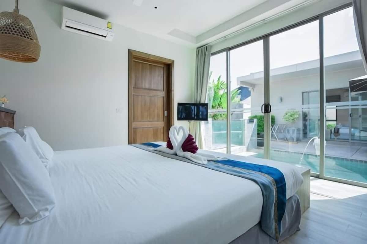 Ein Hotelzimmer mit Bett, Flachbildfernseher, einer Schiebeglastür zu einem Poolbereich und einer Holztür.