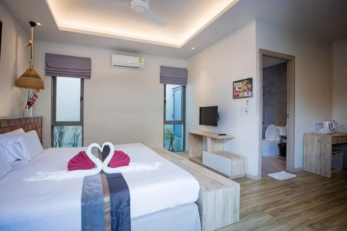 Ein modernes Hotelzimmer mit einem großen Bett, einem Schreibtisch, einem Fernseher und einem sichtbaren Badezimmer hinter einer offenen Tür.