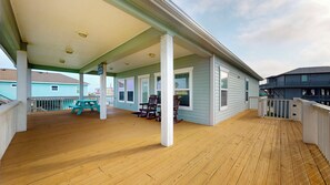 Een overdekt houten terras met een picknicktafel, schommelstoelen en uitzicht op omliggende huizen.