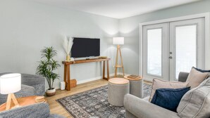 Un salon moderne avec un téléviseur à écran plat, un meuble TV en bois, une lampe sur pied, un canapé gris, un tapis à motifs et une plante en pot.