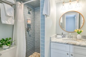 A bathroom with a shower, a sink with a marble countertop, a round mirror, and a potted plant.