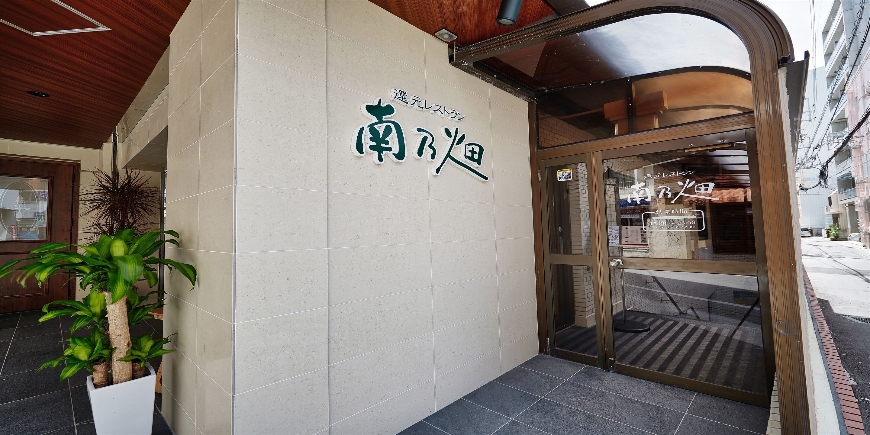 A hotel entrance with a sign in Japanese, a potted plant, and a tiled floor.