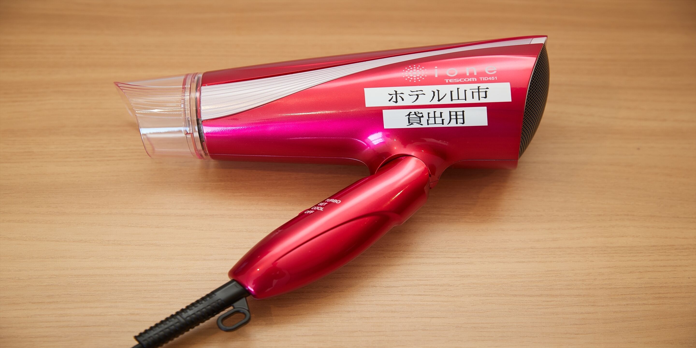 Un secador de pelo rojo con una cubierta de plástico transparente y una etiqueta con texto en japonés.