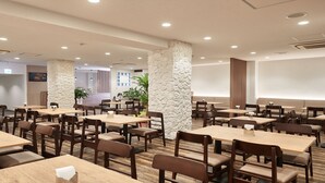 Um restaurante moderno com mesas e cadeiras de madeira, pilares de pedra e iluminação embutida.