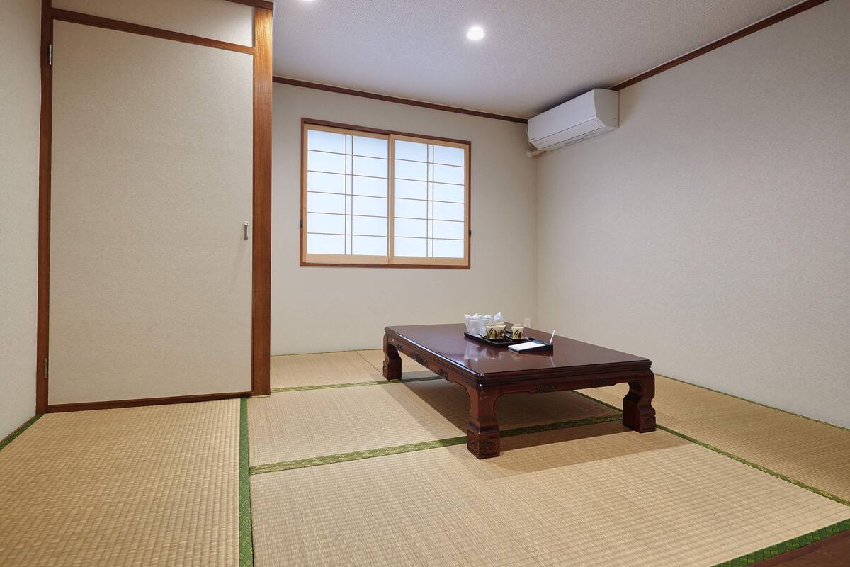 A traditional Japanese room with tatami flooring, a sliding door, a window, and a table with a tray of items.