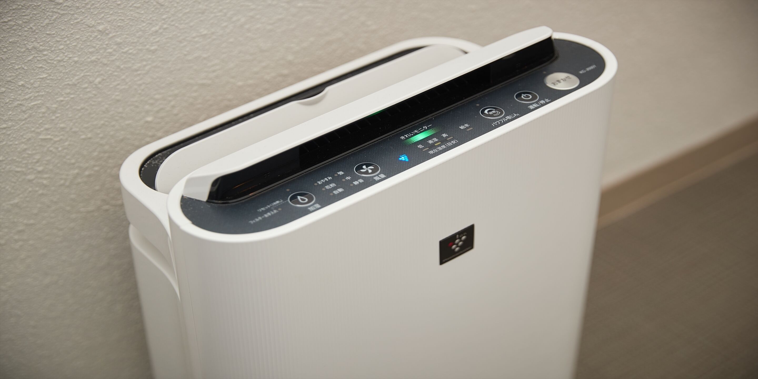 A white, modern, wall-mounted air purifier with a digital display and control panel.