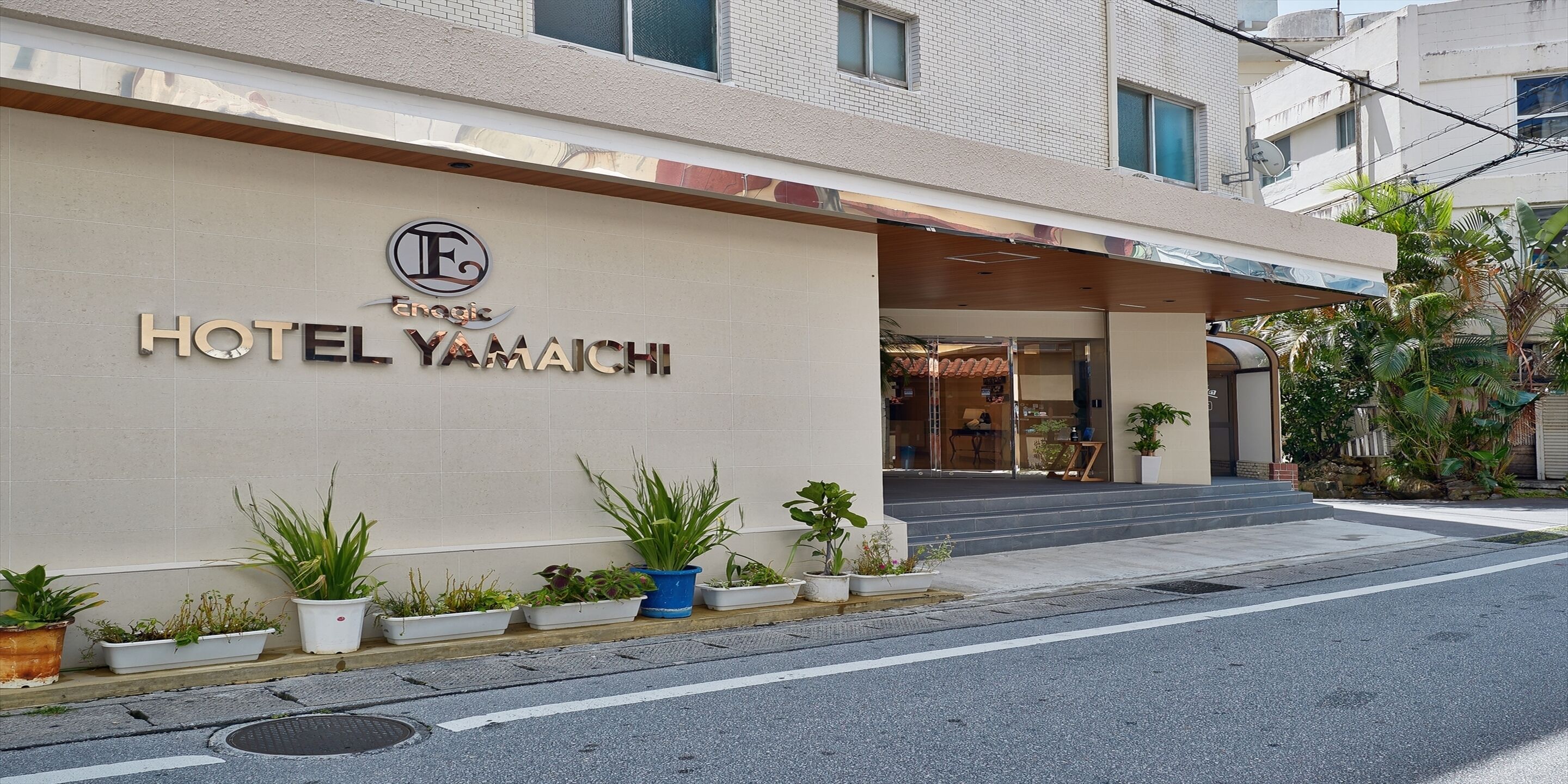 A hotel entrance with a sign reading "HOTEL YAMAICHI" and a logo above it. There are potted plants in front of the entrance.