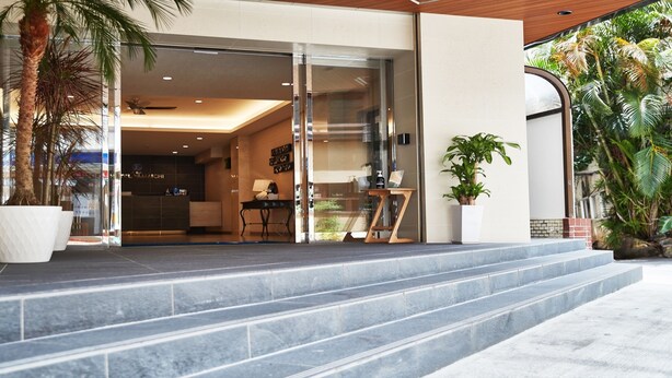 Entrada moderna de edifício com porta de vidro, escadaria e plantas em vasos.
