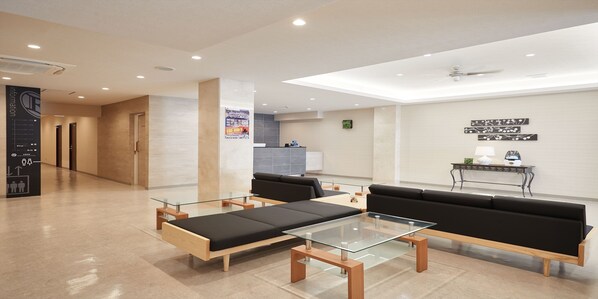 A modern hotel lobby with a reception desk, black sofas, and a glass-top coffee table. - Enagic Hotel Yamaichi (Naha)