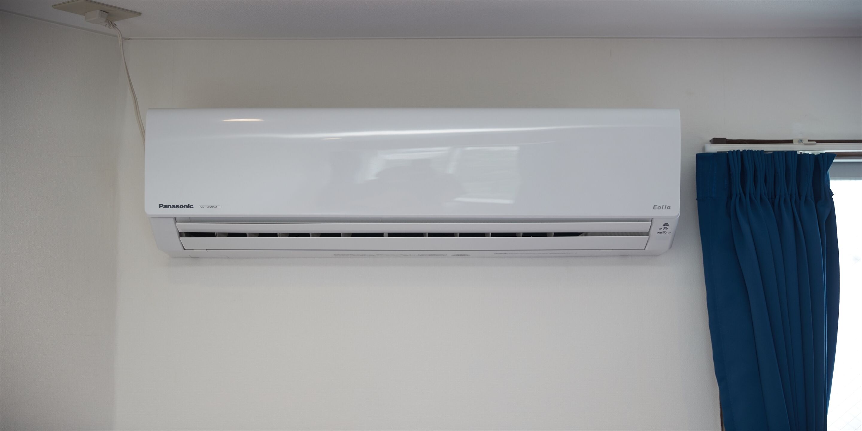 Un aire acondicionado blanco Panasonic montado en la pared de una habitación con ventana y cortina.