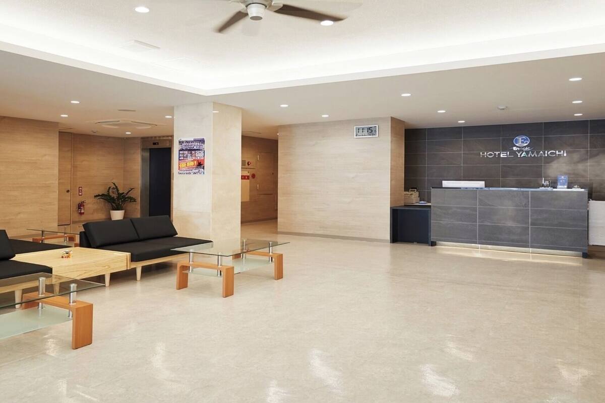 A hotel reception area with a reception desk, a digital clock, and a seating area with sofas and tables.