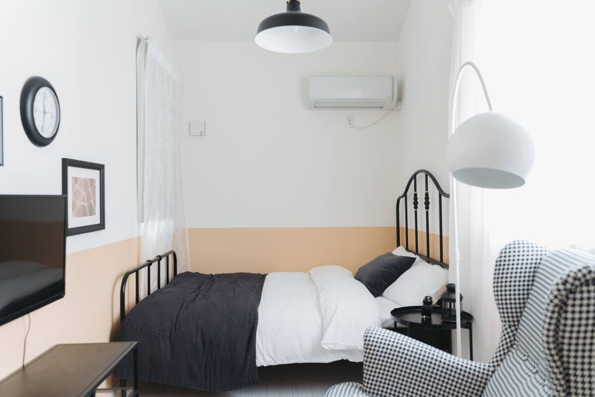 A small, neatly arranged bedroom with a single bed, bedside table, and a chair.