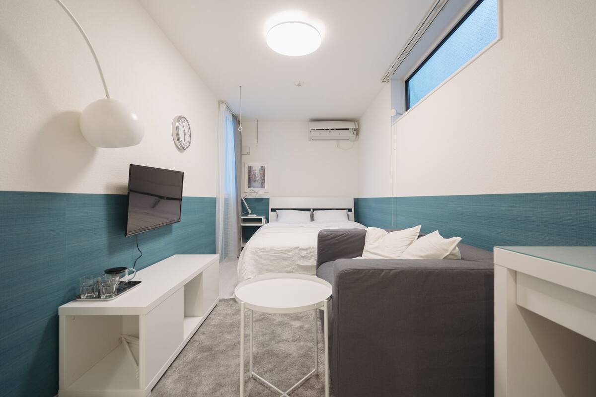 A compact hotel room with a bed, a desk, a chair, a small table, and a TV.