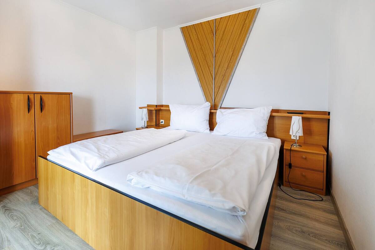 Un lit bien fait, avec du linge de lit blanc, une tête de lit en bois, une table de chevet avec une lampe et une armoire.