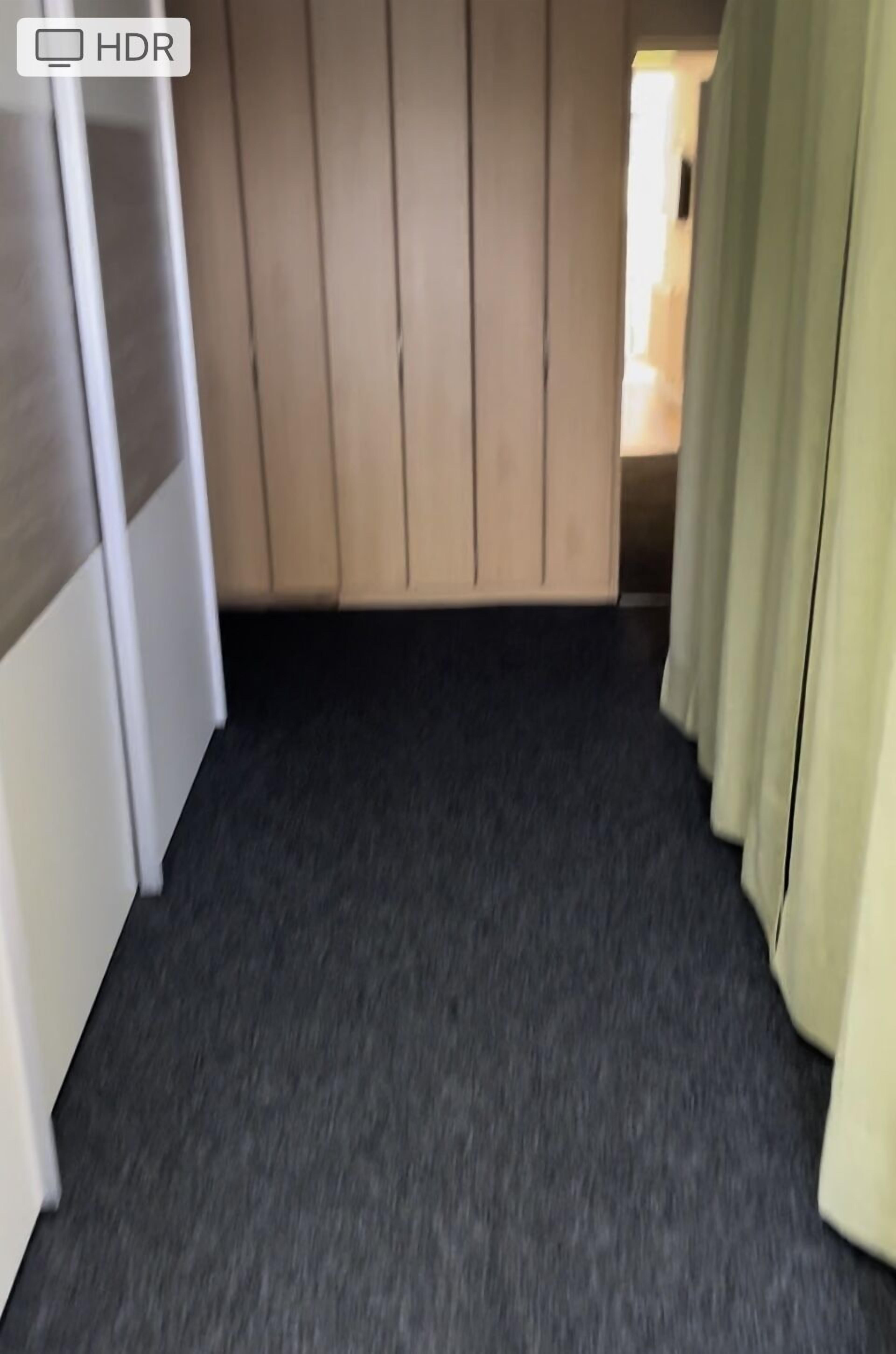 A narrow hallway with a dark floor, light-colored walls, and a door at the end.