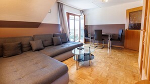 Een moderne woonkamer met een hoekbank, een glazen salontafel en een eethoek met tafel en stoelen.