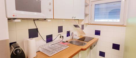 A compact kitchen with white cabinets, a microwave, a sink, and a window.