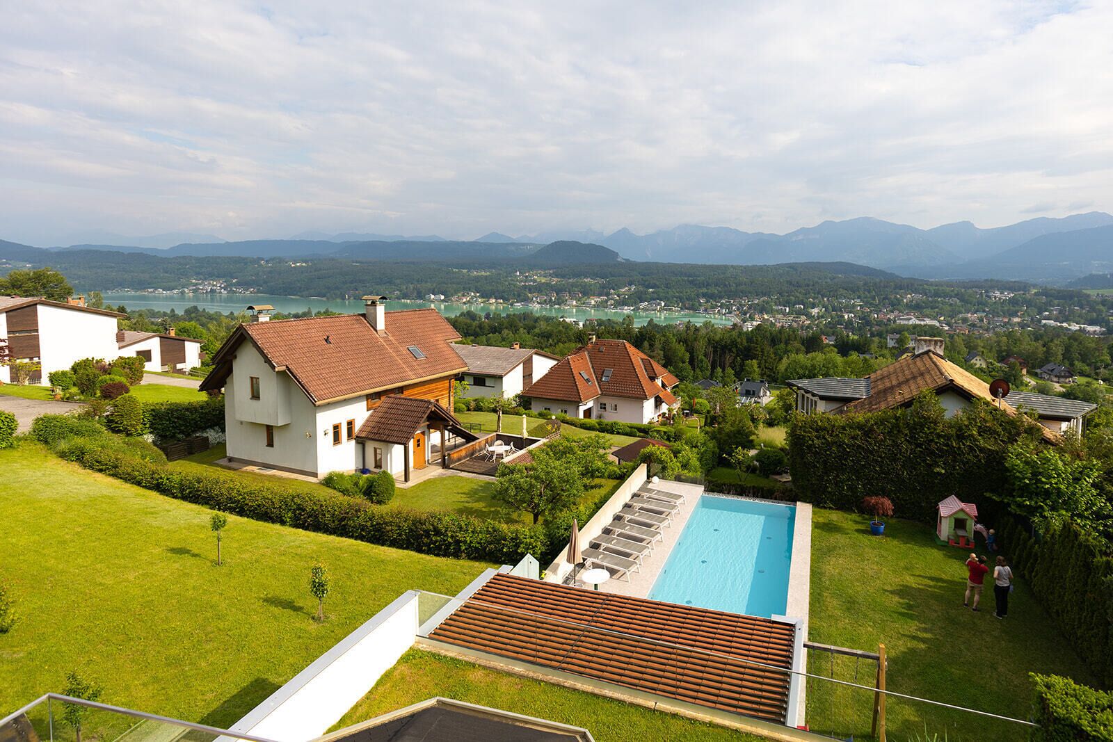 A residential area with houses, a swimming pool, and a view of mountains and a lake.