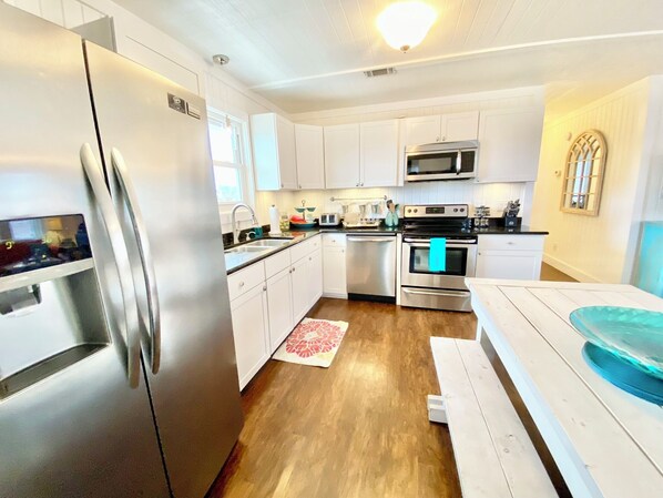 A modern kitchen with stainless steel appliances, white cabinetry, and a wooden floor.