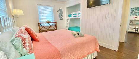 A bedroom with a bed, a ceiling fan, a TV, and a bunk bed.