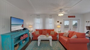 Una sala de estar con una televisión, dos sofás naranja, una mesa de centro blanca y un mueble turquesa.